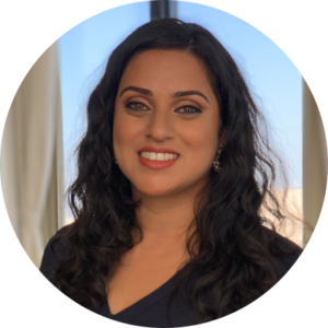 Aparna Kothary, with shoulder-length hair and a black top, smiling against a window